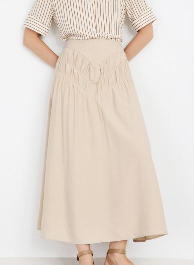 Mujer vistiendo falda midi beige con canesú en pico y detalle de frunces delanteros.